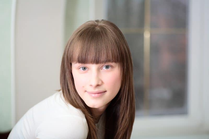 Portrait of a relaxed young woman smiling with hand on chin on sofa in living room